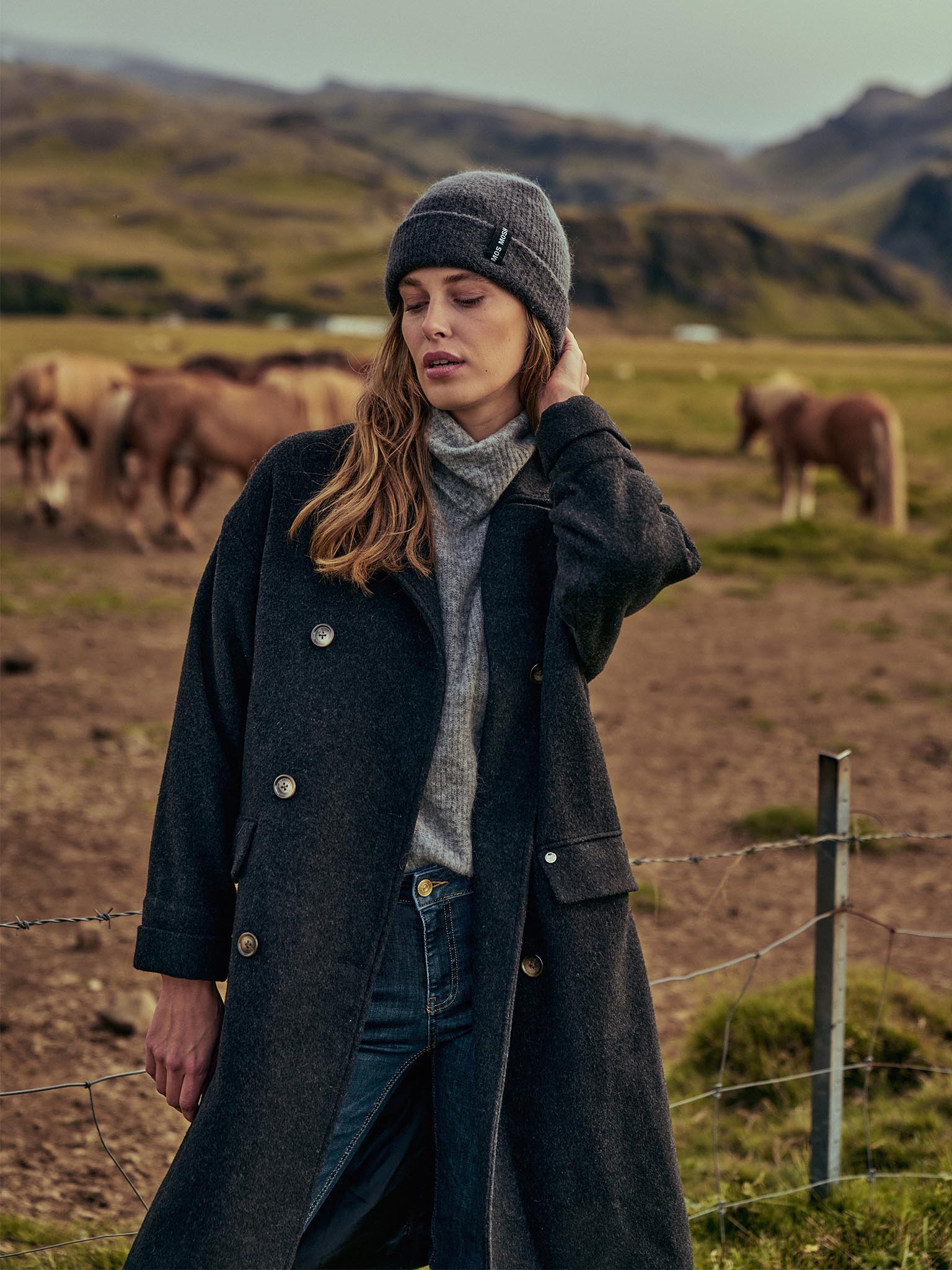 Lady standing in a horse field wearing warm clothes including Mos Mosh Venice Wool Pavement Coat