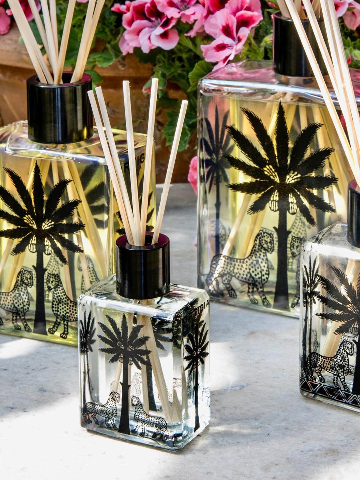 Ortigia Fico Palma Diffusers Collection lined up on table in front of flowers